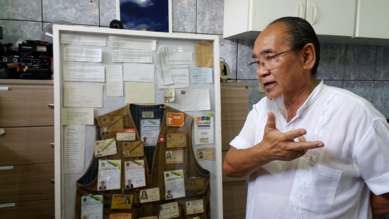 Roberto Higa ao lado de quadro onde guarda todos as credenciais de trabalhos anteriores